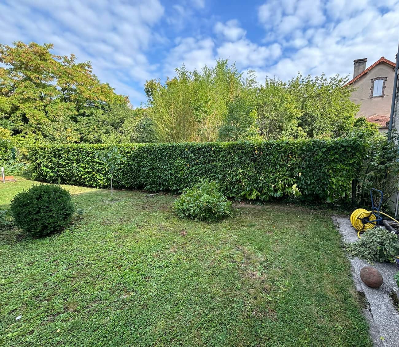 Jardin privé à Cunfin avec une haie parfaitement taillée et une pelouse entretenue.
